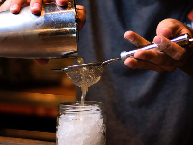 straining a cocktail into a glass jar